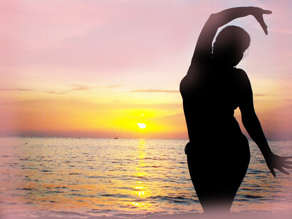 Standing in front of the sea, a woman dances in the sunshine
