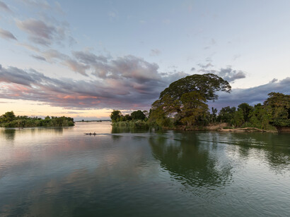 Una piragua navegando por el Mekong al atardecer, con nubes rosadas, en Don Det, Laos