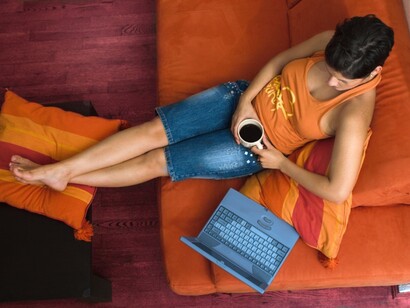 Una chica tumbada en el sofá mientras navega por internet con su portátil