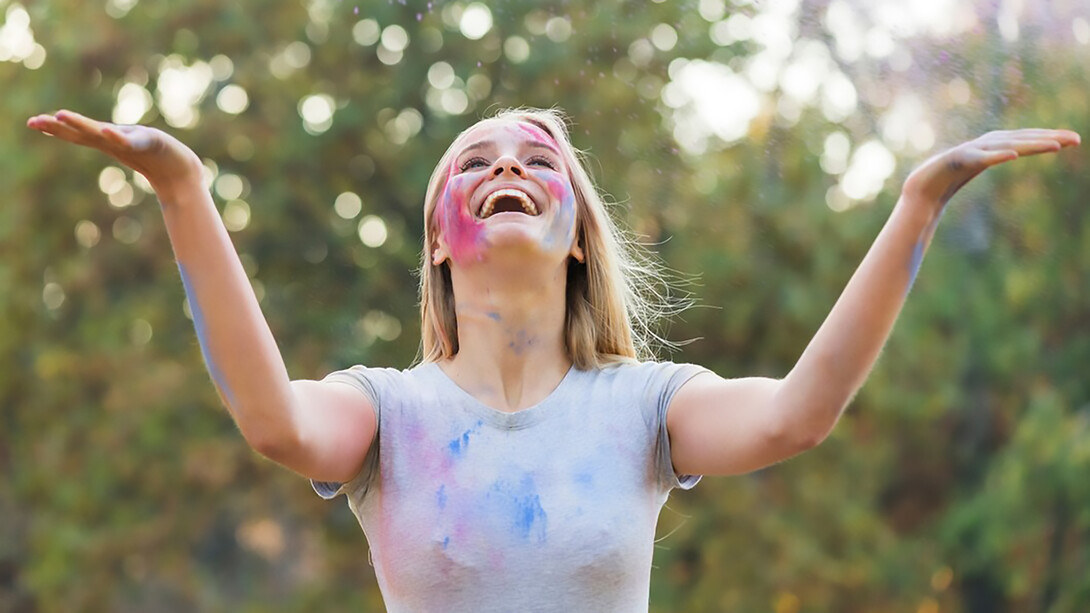 Happy woman enjoying a playful moment with powdered color, celebrating the joy of life and the connection between happiness and physical well-being
