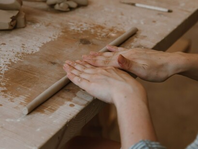 Uma pessoa trabalha a massa com as mãos sobre uma mesa, concentrando-se nos movimentos de modelagem. Assim como na cerâmica artesanal, a repetição dos gestos e o controle da pressão são fundamentais para alcançar a forma desejada