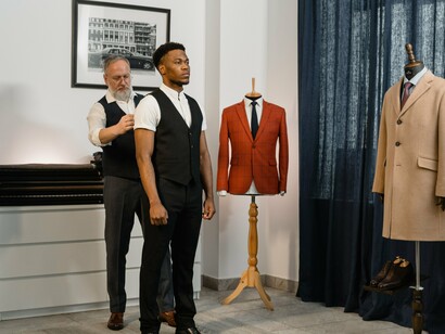 A tailor carefully measuring a person in a professional fitting studio, representing the technical precision and real-world expertise required to turn a fashion concept into a wearable garment