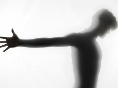 Silhouetted hands in a studio as a figure dissolves, capturing the quiet transformation of identity