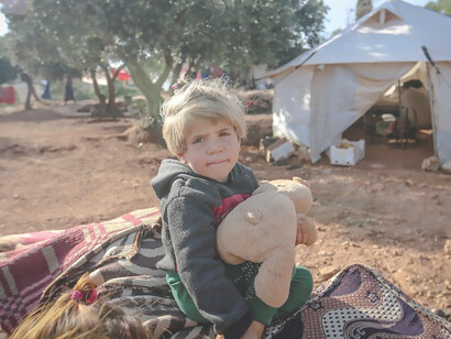 Within the Idlib Governorate of Syria, a touching moment is captured as a resilient young girl finds solace and joy in a simple toy, embodying hope amid the hardships of her life within a refugee camp