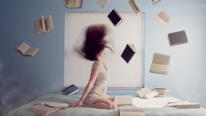 Woman sitting on bed with flying books