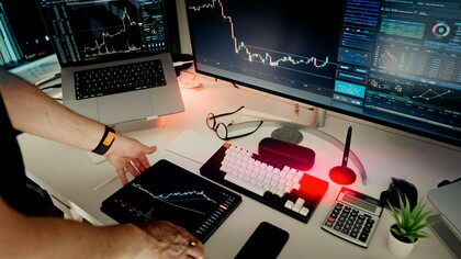Un grand moniteur principal et un ordinateur portable surélevé présentent des courbes de tendance et des données de marché lumineuses