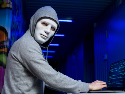 A masked hacker in a hoodie using a computer to carry out a cyber attack