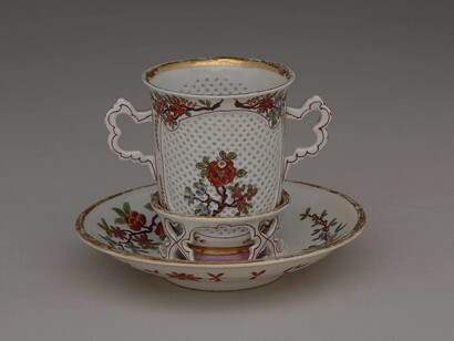 Vienna, Du Paquier, 1735. La ricercatezza degli effetti e l’esaltazione della traslucidità della porcellana hanno il loro apice in questa tazza trembleuse, realizzata a Vienna nella manifattura Du Paquier intorno al 1725-1730. Le pareti della tazza sono state lavorate a crudo creando piccoli fori dalla forma roimboidale, poi riempiti dalla vetrina traslucida, in modo da poter bere dalla tazza mantenendo l’effetto di un pizzo. 
