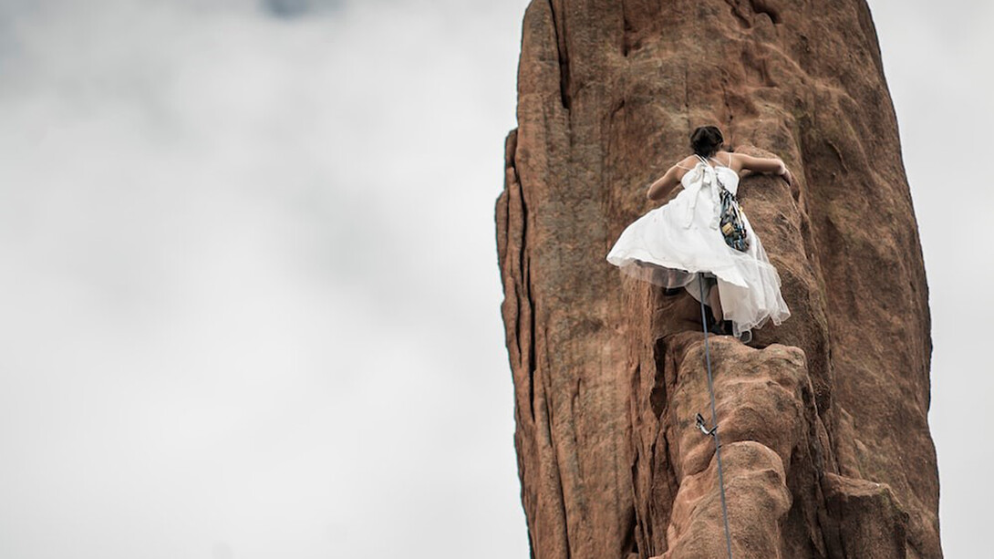 In her white wedding dress, the woman embodies the essence of feminine consciousness as she climbs the brown rock under the pure white sky, symbolizing her innate strength, determination, and the sacred union of her inner and outer worlds