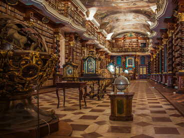 The grand Baroque Library of the Klementinum, Prague, lined with ancient books, ornate balconies, globes, and painted ceilings, representing the centuries-old pursuit of knowledge
