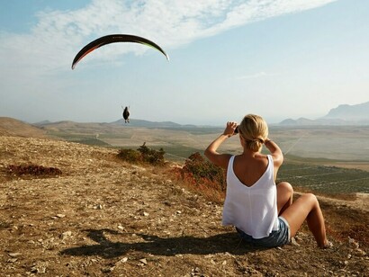 Bathed in soft sunlight, a serene young blonde woman stands on a quiet hilltop, embracing the peacefulness of nature