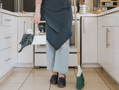 A woman stands gracefully in her kitchen, firmly gripping a broom