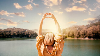 Experience a symbolic moment of self-discovery as a woman creates heart-shaped hands against a sunset backdrop in this captivating image