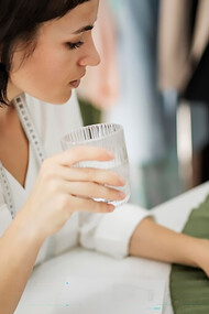 A female tailor takes a refreshing water break while gently touching a bio-based fabric, showcasing her dedication to sustainable materials in the fashion industry
