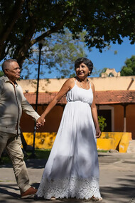 A happy elderly Indian couple stands smiling outside their home, radiating warmth and togetherness
