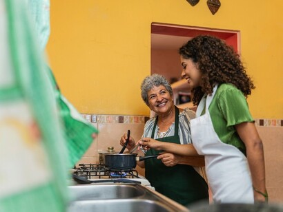 A grandmother teaching a young woman how to prepare a traditional family dish in the kitchen