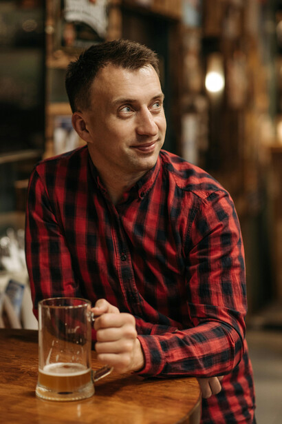 Wearing a checkered shirt, a man holds a beer glass during a tasting session