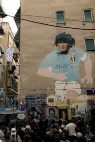 A large mural depicting a man wearing a helmet on the side of a building at Largo Maradona; Murales Maradona in Naples, Italy 