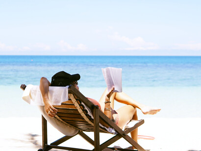 A woman reading a book on the beach while on vacation in Thailand