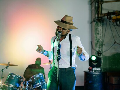 Man wearing a hat singing with a band at a classic-style concert, drums and live energ