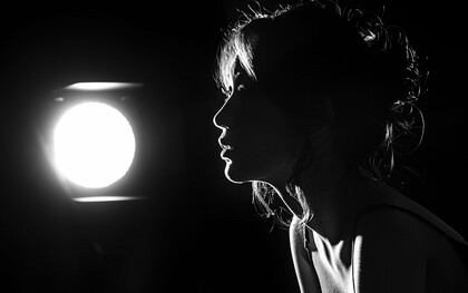 A silhueta de uma mulher emerge diante de uma única luz, enquanto o resto permanece em sombra. Em “Joshua”, Elsa Mangue transforma esse contraste entre escuridão e claridade numa recusa que também é sobrevivência. A imagem ecoa a força íntima de quem fecha a porta para não morrer por dentro
