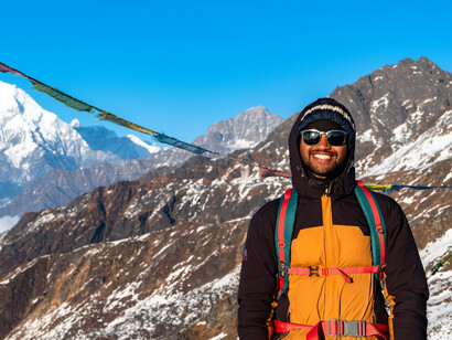 A man in an orange and black jacket, wearing black goggles, at Gosaikunda, Nepal