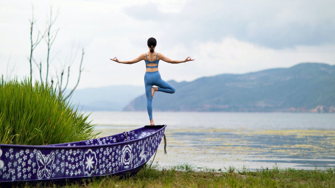 Postura de yoga em meio a natureza em cima de um barco azul próximo ao rio