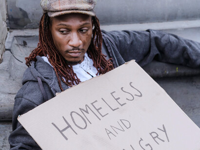 Un homme en situation de grande précarité, assis dans la rue avec une pancarte exprimant son besoin urgent de nourriture et de logement
