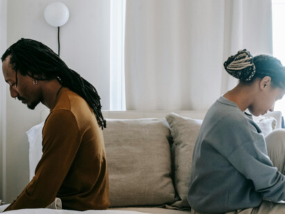 A couple seated apart on a bed, suggesting conflict or unresolved issues