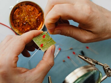 Hands assembling electronic components on a workbench, representing the human effort behind increasingly powerful technologies