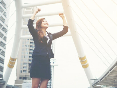 Happy and successful businesswoman overlooking the city center with hands raised, celebrating career development and professional success