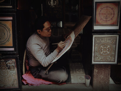 An Asian man sits on the ground working on his art and creativity 