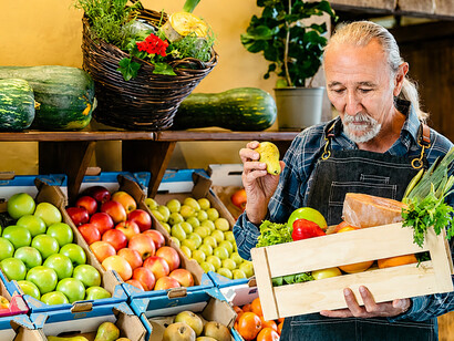 Greengrocer preparing a display of fresh produce, including colorful fruits and vegetables, at a neighborhood grocery store