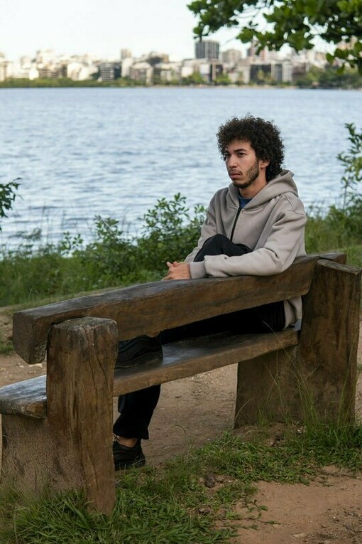 A young man sitting alone on a park bench beside a lake, representing the loneliness and uncertainty that can accompany the fear of abandonment