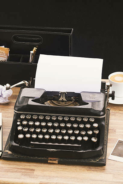 On a wooden desk, an old typewriter is placed next to a collection of historical diaries and literary archives