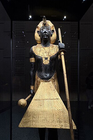 Life-sized guardian statue of King Tutankhamun wearing the Khat headdress, gilded collar, and kilt, holding a mace and staff, on display at the Egyptian Museum in Cairo, Egypt