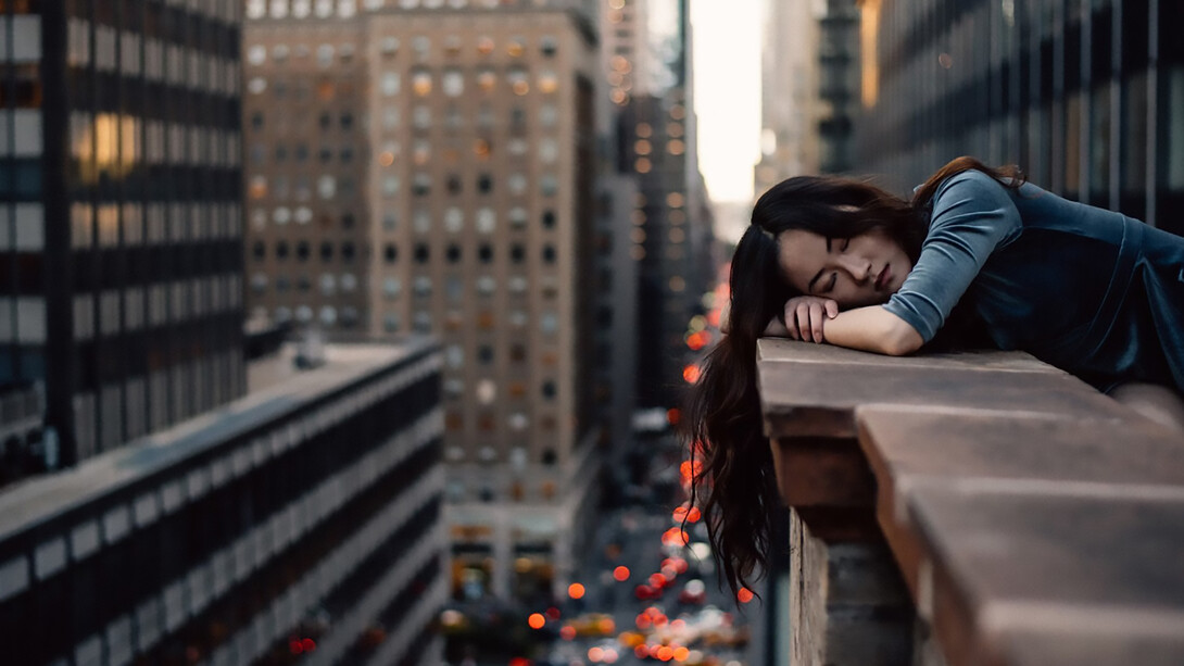 A young woman leans on a rooftop railing in New York City, overwhelmed and exhausted — a quiet moment of burnout in the pursuit of unpaid opportunity