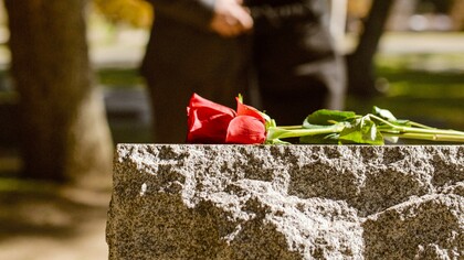Rosa em cima de um túmulo e pessoas de luto ao fundo