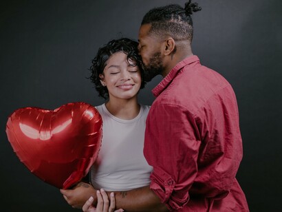 Homem beijando sua mulher enquanto segura um balão vermelho em forma de coração