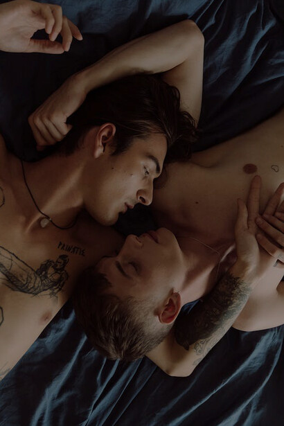 A pair of gentlemen cuddled in bed, sharing an affectionate moment