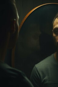 A dimly lit portrait of a man staring into a mirror, his reflection revealing a shadowed, contemplative expression, captures the essence of shadow work—facing the parts of ourselves we often ignore