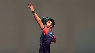 Athletic padel player getting into position for a shot on an indoor glass court