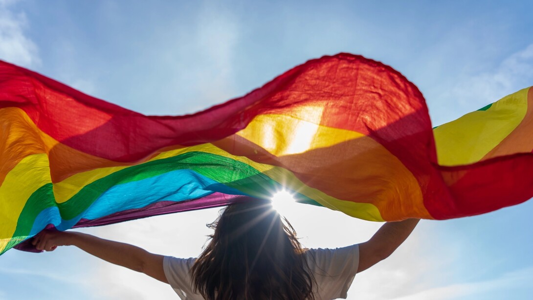  A young woman waving LGBTQIA+ flag under the sky