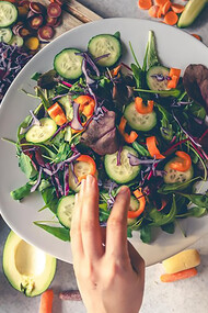 Female hands holding a bowl of vegan salad with fresh vegetables 