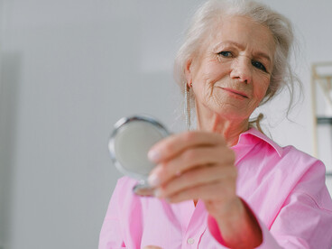 An elderly woman holding a mirror as she reflects on the passage of time