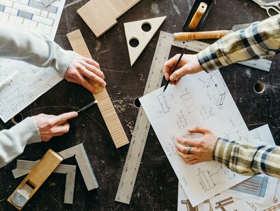 Detailed building plans surrounded by engineering tools, reflecting the disciplined thinking required to create lasting economic success
