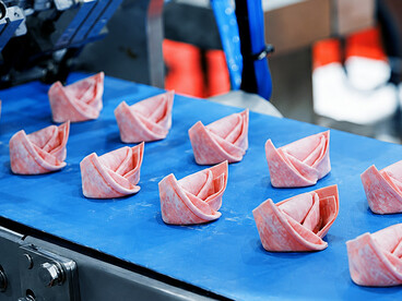 Industrial robots handle semi-finished croissants on a production line, transferring them from conveyor belts into containers with speed and precisio