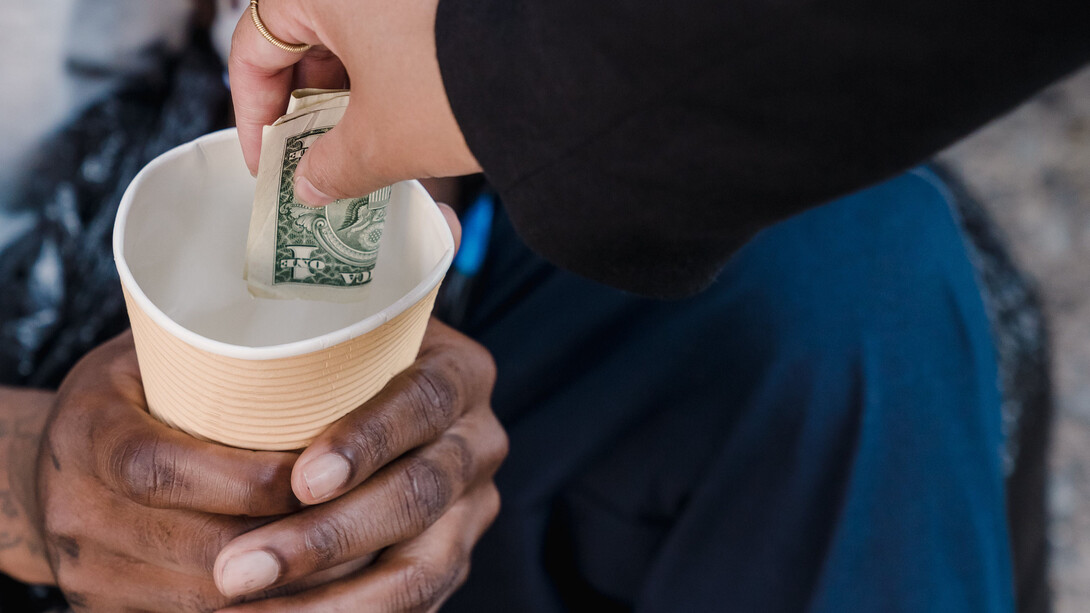 Mão doa um nota de dinheiro para pessoa desempregada e em situação de desabrigo
