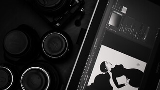 A black and silver DSLR camera placed beside a tablet, where someone is drawing—capturing a moment of creativity in action