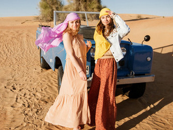 In the United Arab Emirates, two women stand by a blue Land Rover in the desert during a safari